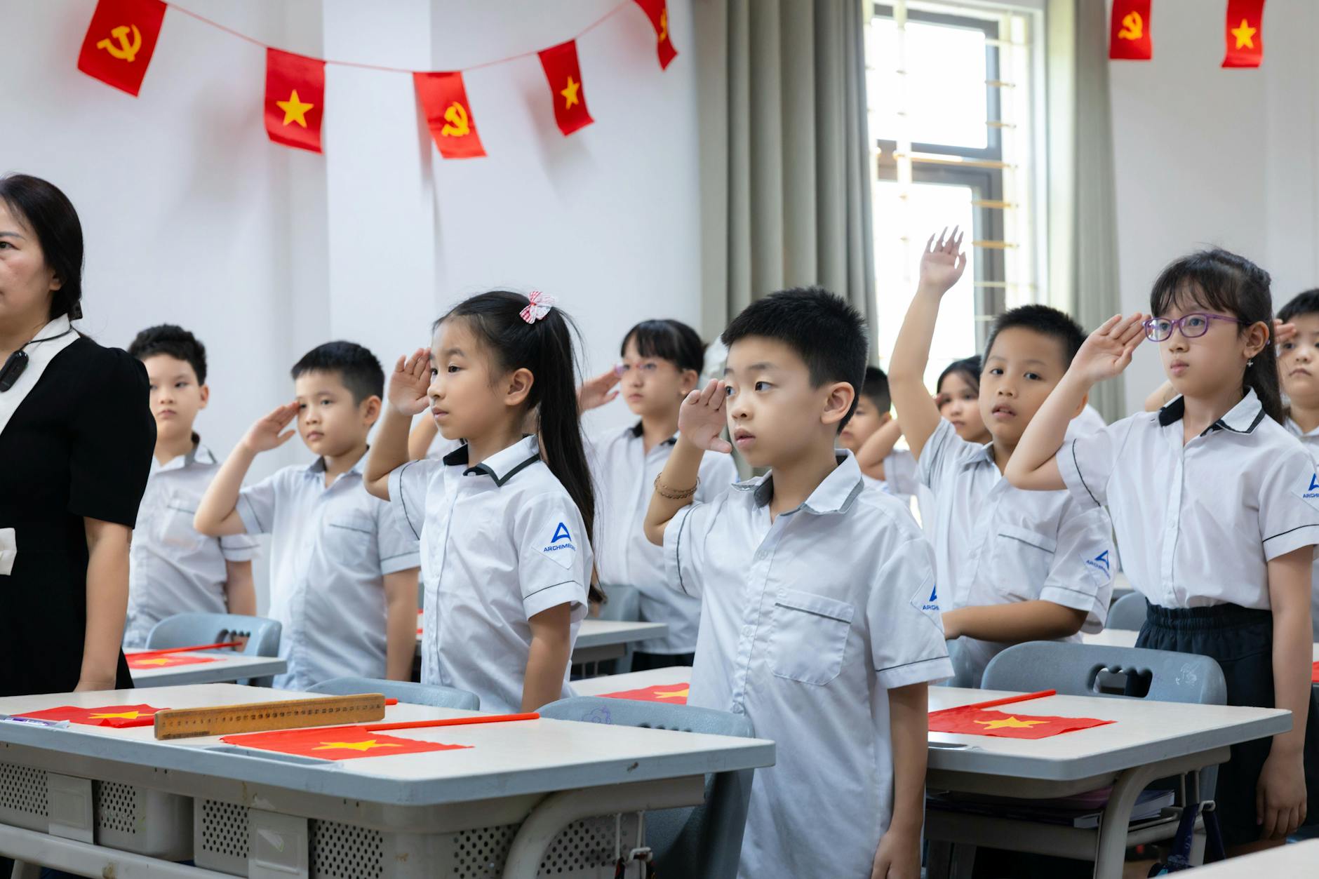 Wietnamscy uczniowie w białych mundurkach salutują do flag w klasie