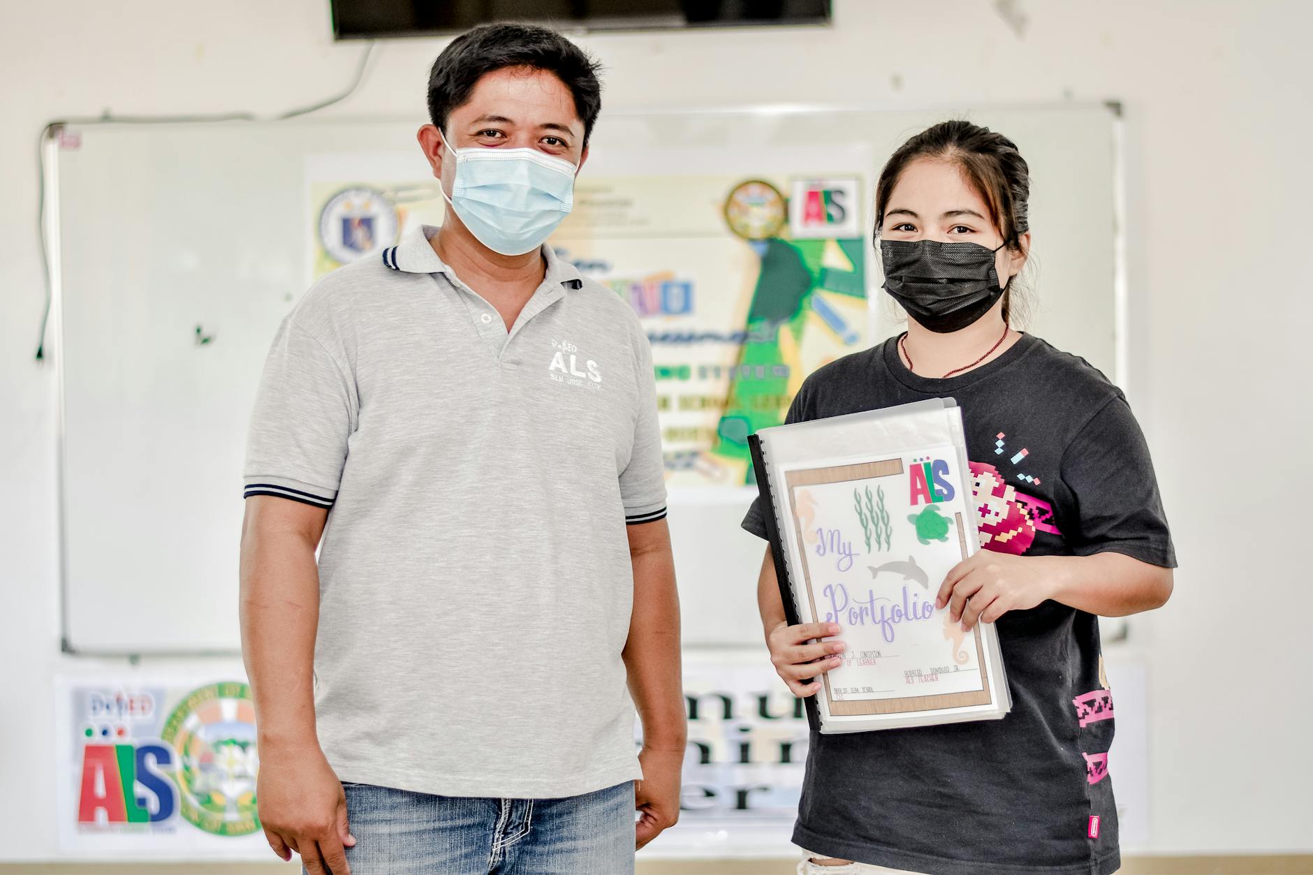 Dwóch azjatyckich uczniów w maseczkach prezentuje materiały edukacyjne