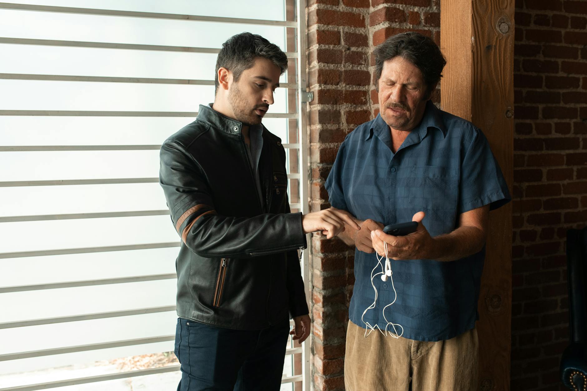 Dwóch mężczyzn w domu rozmawia, spoglądając na ekran smartfona