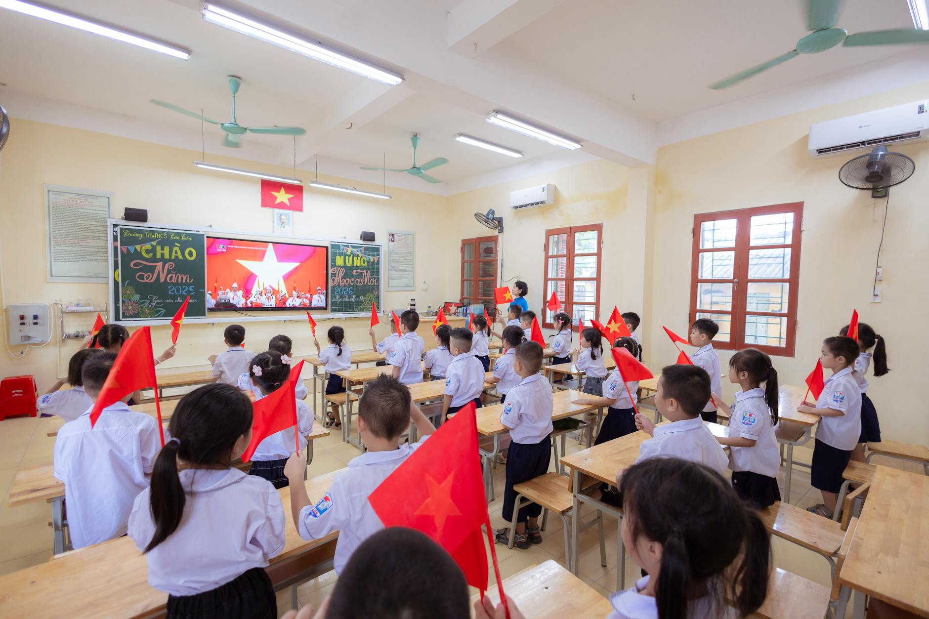 Uczniowie w klasie machają narodowymi flagami podczas szkolnej uroczystości